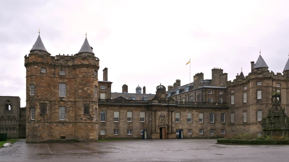 Palace of Holyroodhouse 的石砌正立面与两座圆塔围住雨后的前庭。