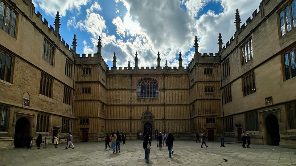 Bodleian Library 的 Old Schools Quadrangle 被金色石墙、尖塔和拱窗围合，中央入口正对庭院。