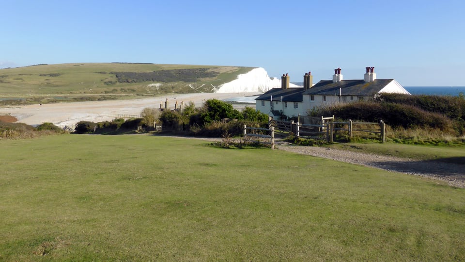 从 Seaford Head 近看 Coastguard Cottages，白垩崖、河口草地与海岸小屋在秋日光线中相接。
