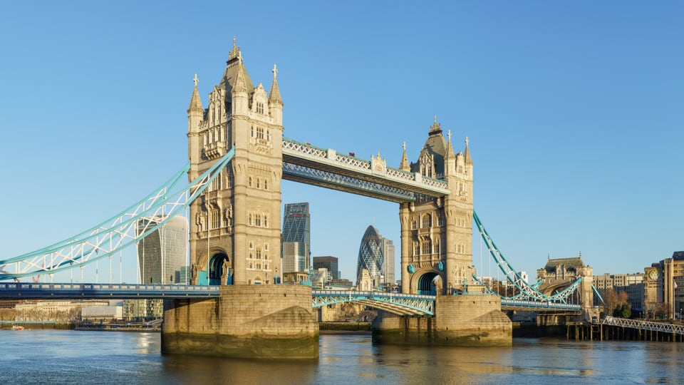 从 Shad Thames 一侧望向 Tower Bridge，两座石塔、蓝色悬索和上层步道横跨泰晤士河。
