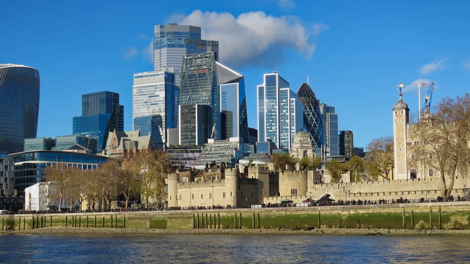 Thames 横过前景，Tower of London 的城墙与 White Tower 立在 City of London 天际线前方。